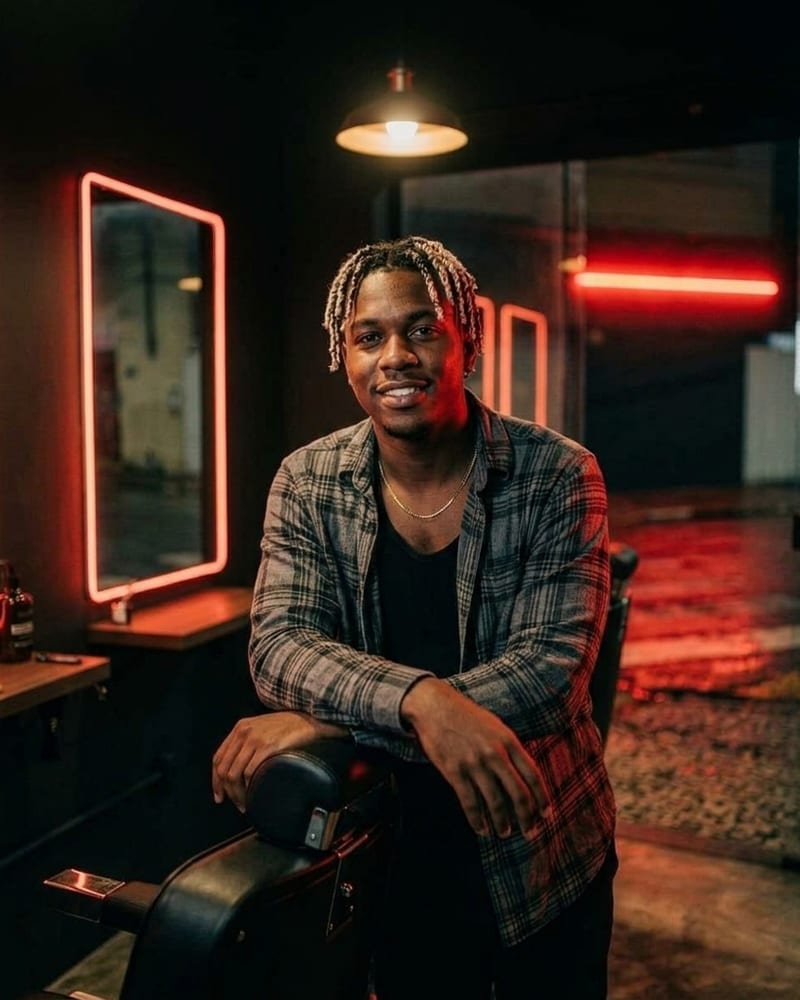 Biel Santos, de twists curtos com pontas platinadas e corrente dourada, com camisa xadrez cinza aberta sobre regata preta