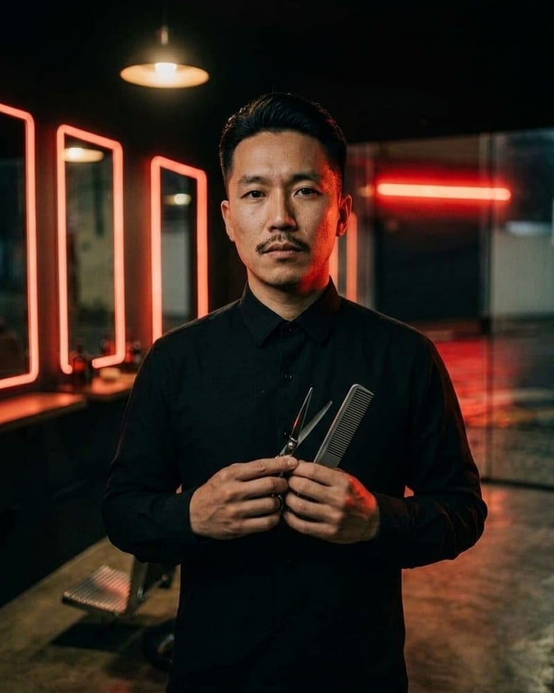 Kenzo Mori, de cabelo liso preto em undercut e bigode fino, com camisa preta abotoada até em cima